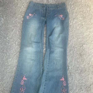Blå jeans med broderade blommor - Snygga blå jeans med broderade rosa blommor och fåglar på benen. Jeansen har en rak och lite vidare passform och är tillverkade i klassiskt denimtyg. Perfekta för dig som vill sticka ut med coola detaljer och färgglada broderier.