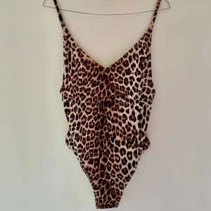 Leopardmönstrad body/baddräkt - Snygg body/baddräkt med leopardmönster och smala axelband. V-ringad framtill, djup i ryggen och högt skuren vid benen för en trendig look. 