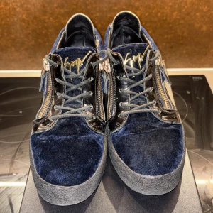 Blå sammetssneakers från Giuseppe Zanotti - Snygga sneakers i mörkblå sammet och svart skinn från Giuseppe Zanotti. Skorna har guldfärgade dragkedjor på sidorna, snörning och en svart gummisula. Lyxig känsla med coola detaljer och ikonisk logga på plösen. 