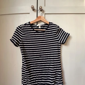 Randig t-shirt från H&M, svart/vit - Snygg svart och vit randig t-shirt från H&M i storlek S. Klassisk modell med rund hals och korta ärmar. Tillverkad i mjuk bomull som är skön mot huden. Perfekt till jeans eller shorts för en chill look.