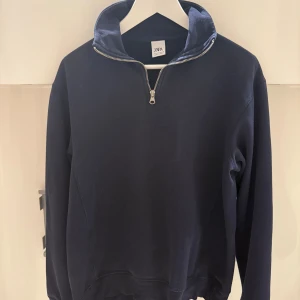 Mörkblå half zip tröja från Zara - Mörkblå långärmad tröja från Zara med hög krage och half zip-dragkedja. Tröjan är i mjuk bomull och har en clean, stilren look som passar perfekt till jeans eller joggers. Enkel och snygg design utan tryck eller mönster.