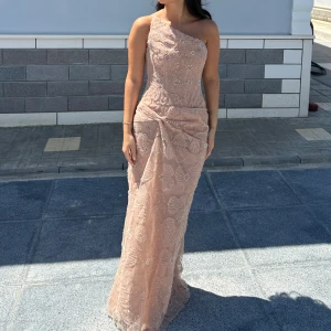  långklänning med blommor - Skräddarsydd Elegant långklänning, egendesignad i Kosovo . Klänningen har ett vackert blommigt mönster med pärldetaljer och är figurnära med drapering vid höften. Perfekt för dig som vill sticka ut med en sofistikerad look. Nypris 7000kr använd endast en gång under några timmar