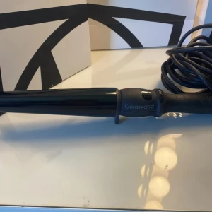 CeraWand Locktång - CeraWand locktång med keramisk beläggning för skonsam styling. Svart design, lång sladd och ergonomiskt handtag. Produkten ser ut att vara i gott skick med mindre ytliga repor på handtaget. Perfekt för att skapa vackra lockar snabbt och enkelt.