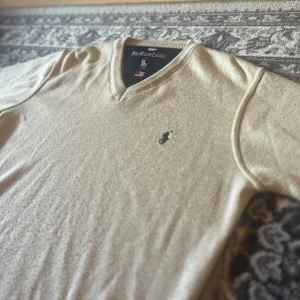 Beige v-ringad tröja Polo Ralph Lauren - Bra skick. Köpte för 1800 säljer för 400kr Snygg beige v-ringad tröja från Polo Ralph Lauren med klassisk broderad logga på bröstet. Tröjan är långärmad och har ribbade muddar vid ärmslut och nederkant. Perfekt för lager-på-lager och stilrena outfits.