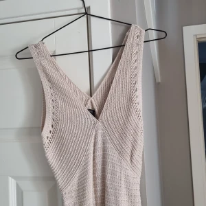 Beige stickad långklänning Lindex XS - Supersnygg beige stickad långklänning från Lindex i storlek XS. Klänningen är ärmlös med v-ringning och har ett virkat mönster samt fina detaljer nertill. Perfekt för sommarens varma dagar och ger en chill och trendig vibe. Oanvänd.