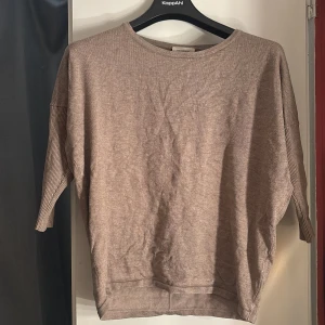 Beige stickad tröja från Freequent - Beige stickad tröja från Freequent i storlek small. Tröjan har trekvartsärmar med ribbade detaljer och en rak, avslappnad passform. Perfekt för lager-på-lager och enkel att matcha med jeans eller kjol.