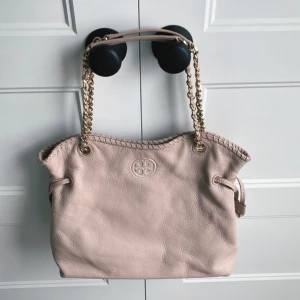 Rosa väska från Tory Burch - Säljer en snygg ljusrosa axelväska från Tory Burch i mjukt skinn. Väskan har kedjehandtag med läderdetaljer, dekorativt flätad kant och det klassiska logotyp-emblemet framtill. 