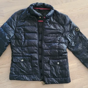 Svart pufferjacka från Gina Tricot - Snygg svart pufferjacka från Gina Tricot i storlek 38. Jackan har quiltad design, dragkedja framtill, två fickor med lock och knapp samt en liten logga på ärmen. Perfekt för kyliga dagar och enkel att matcha med allt.