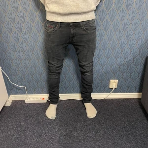 Svarta slim jeans från Tommy Hilfiger - Säljer ett par svarta skinny jeans från Tommy Hilfiger med klassisk femficksdesign och diskret logga på bakfickan. Jeansen har låg midja och är tillverkade i stretchigt bomullsmaterial för en tight passform. Perfekta för dig som gillar en stilren och modern look. W 32 L32