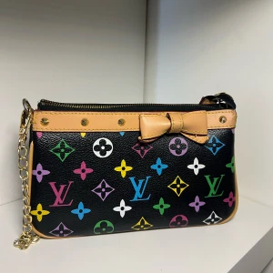 Louis Vuitton svart handväska med rosett - Snygg svart handväska från Louis Vuitton med färgglada loggor och mönster i rosa, blått, grönt, gult, vitt och lila. Väskan har en guldkedja, beige kant och en söt rosett framtill. Perfekt storlek för det viktigaste och stängs med dragkedja.