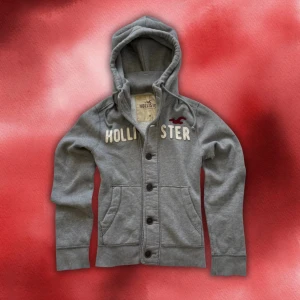 Grå hoodie / cardigan med knappar från Hollister M/L - Grå hoodie / cardigan från Hollister med knappar och broderad logga och text på bröstet | M/L | Vintage och extremt limiterad! | Längd: 65cm Axelbredd: 40cm Armlängd: 70cm
