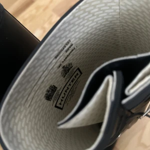 Svarta Hunter stövlar i gummi - Klassiska svarta Hunter stövlar i gummi med justerbart spänne på sidan och rund tå. Perfekta för regniga dagar och festivaler. Snygg logga framtill och slitstark sula för bra grepp. Insidan har ljust mönstrat foder för extra komfort. SÄLJS FÖR 1700kr i butik !!