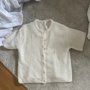 Beige kofta i ullmix från Gina Tricot - Superfin beige kofta från Gina Tricot i mjuk ullblandning. Koftan har korta ärmar, ribbad struktur och knäppning framtill med flera knappar. Perfekt att slänga över en topp för en chill och stilren look. Strl M