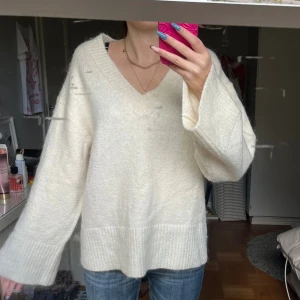 Vit stickad v-ringad tröja från Gina Tricot - Mysig vit stickad tröja från Gina Tricot med breda ribbade muddar och v-ringning. Tröjan har en relaxed fit och långa ärmar, perfekt för lager-på-lager. Enkel att styla med jeans eller kjol för en chill look.