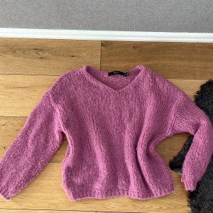 Rosa stickad tröja från Vero Moda - Mysig rosa stickad tröja från Vero Moda med v-ringad hals och långärmad modell. Tröjan har en fluffig känsla och är perfekt för lager-på-lager under kyliga dagar. Passformen är normal och materialet känns mjukt mot huden.