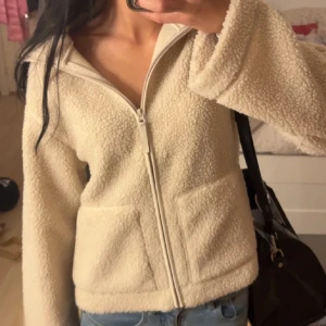 Beige teddyjacka H&M - Mysig beige teddyjacka med hel dragkedja framtill och två stora fickor. Jackan har en rak passform och är tillverkad i fluffigt fleece-material. Perfekt för lager-på-lager och chill vardagsstil.