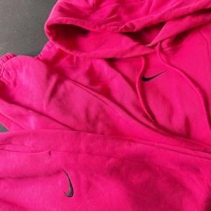 Ceriserosa Nike hoodie med huva - Säljer en ceriserosa hoodie och ett par mjukisar till.  Bra skick. Storlek S på byxorna och XS på hoodien  