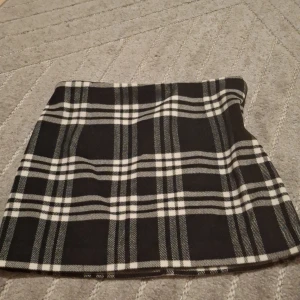 Rutig svartvit minikjol från Gina Tricot - Supersnygg kort kjol från Gina Tricot i svartvitt rutigt mönster. Kjolen har klassisk A-linjeform och stängs med dragkedja och knapp i sidan. Perfekt för att skapa en cool och trendig look. Dragkedjan hakar upp sig men knappen funkar.