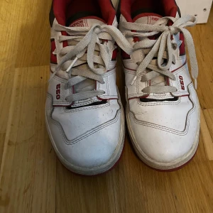 New Balance 550 vita och röda sneakers - Säljer ett par New Balance 550 sneakers i vitt och rött med svarta detaljer. Klassisk retrodesign med snörning, rund tå och platt sula. Ovandel i skinn och syntet, ikonisk N-logga på sidan och broderad NB-logga på hälen. Perfekta för dig som gillar streetwear. Bra skick 