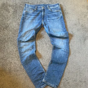 Blå jeans från Gant - Säljer ett par klassiska blå jeans från Gant med fem fickor och snygga kontrastsömmar. Jeansen har normal passform och raka ben, tillverkade i mjukt bomullsjeans-tyg. Man kan ändra storleken i midjan med spännen i byxorna!Perfekta för dig som gillar stilrena och tidlösa jeans med diskret Gant-logga på bakfickan. Pris kan diskuteras vid snabb affär!