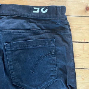 Svarta dondup george jeans - Svarta dondup George jeans  med klassisk femficksdesign och diskret broderad detalj på bakfickan. Jeansen har en smal passform och är tillverkade i ett stretchigt bomullsmaterial för extra komfort. Perfekta för dig som gillar en tajt siluett.