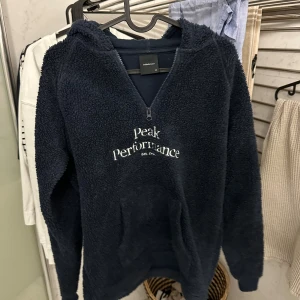 Mörkblå fleece hoodie Peak Performance - Mysig mörkblå hoodie från Peak Performance i fleece med broderad logga på bröstet. Tröjan har half zip, huva och en stor magficka. Perfekt för kyliga dagar och riktigt skön att dra på sig när man vill vara bekväm. Passar S och XS