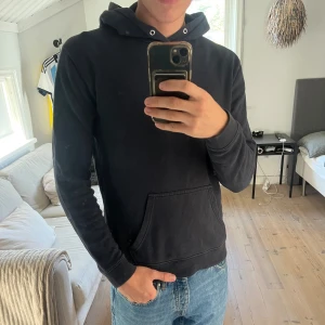 Mörkblå hoodie från NN07 - Säljer en mörkblå  hoodie från NN07 med klassisk känguruficka och huva med snörhål. Tröjan är i mjuk bomull och har en enkel, stilren design som passar perfekt till jeans.