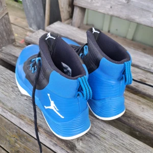 Blåa Jordan basket sneakers - Säljer ett par blåa och svarta Jordan basket sneakers med vit Jumpman-logga på sidan. Skorna har snörning, högt skaft och vit sula med tydligt mönster för bra grepp. Ovandelen är i syntetmaterial och textil, perfekt för dig som gillar sportig stil.
