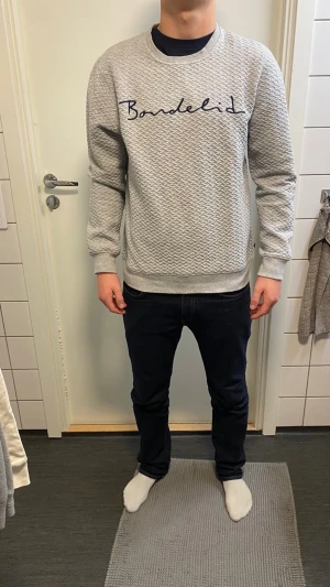 Grå mönstrad tröja från Bondelid - Säljer en grå sweatshirt från Bondelid med diskret mönster och broderad logga framtill. Tröjan har rund halsringning, långa ärmar och ribbade muddar. Perfekt för dig som gillar stilren och bekväm design.