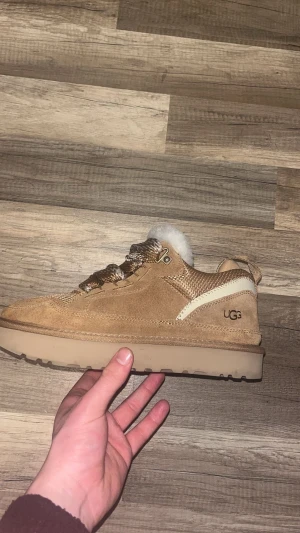 UGG sneakers med fårull och mocka - Säljer ett par snygga UGG sneakers i beige mocka med stickade detaljer och fluffig vit fårull på insidan. Skorna har grova snören, platt sula och UGG-logga på sidan. Perfekta för höst och vinter när du vill hålla stilen och värmen. storleken passar både 44-45. Pris kan diskuteras vid snabb affär.
