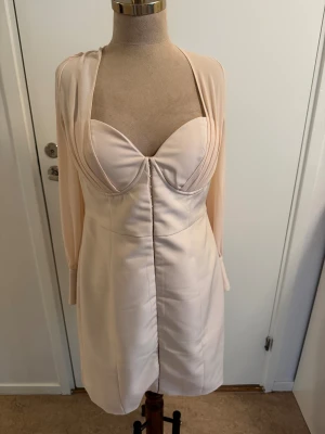 Ljusrosa kort klänning Lavish Alice - Supersnygg ljusrosa kort klänning från Lavish Alice med långärmade transparenta ärmar, markerad byst och djup v-ringning både fram och bak. Klänningen har knappar vid ärmsluten och en figurnära passform som ger en elegant siluett.