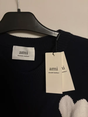 Ami tröja - Snygg mörkblå stickad tröja från Ami Alexandre Mattiussi med vit hjärtapplikation och bokstaven A på bröstet. Tröjan har rund hals och långa ärmar, perfekt för dig som gillar stilrena detaljer och vill ha något som sticker ut. Helt ny prislapp kvar