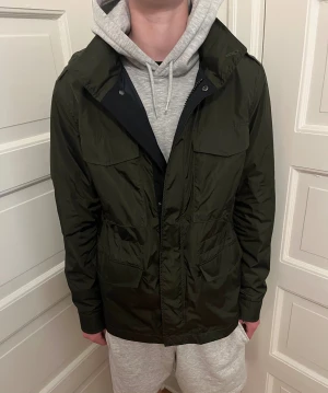 Field jacka - Field jacket från märket Hugo Boss, storlek 48 och är lite stor för mig som är 180 cm, super bra skick, justerbar i midjan och innerfickor finns, färgen inuti jackan är mörkblå och där med luvan som går att ta ut, jackan är ganska tunn så passar perfekt med väst under, skriv vid frågor!