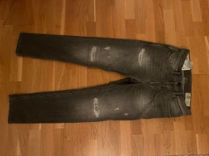 Grå tapered jeans från Diesel - Snygga grå jeans från Diesel, modell D-Eetar med tapered passform. Jeansen har slitna detaljer framtill och klassisk femficksdesign. Materialet är stretchigt denim som ger skön komfort och bra rörelsefrihet. Perfekt för dig som gillar en modern och avslappnad stil.