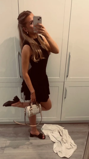 Svart kort klänning med volang - Supersnygg svart klänning med volangkjol och ärmlös design. Den har en figurnära passform upptill och ett lätt utställd kjol med volanger som ger en cool vibe. Perfekt för dig som gillar stilrena och trendiga plagg. Nypris 599kr finns inte att köpa i svergie, den är köpt i Spaniens HM