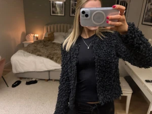 Svart teddyjacka från KappAhl XS - Säljer en svart teddyjacka från KappAhl i storlek XS. Jackan har en fluffig och krullig yta, är kortare i modellen och har långa ärmar. Perfekt för dig som vill ha en mysig och trendig look under kyligare dagar.