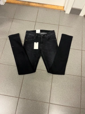 Svarta slimmade jeans Tiger of Sweden W29 L32 - Svarta jeans från Tiger of Sweden med tight passform och smala ben. Klassisk femficksmodell med diskreta detaljer och svart läderpatch bak. Snygg tvätt och stilren look, perfekta till sneakers eller boots. W29 L32