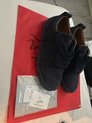 Mörkblå sneakers från Christian Louboutin - Snygga mörkblå sneakers från Christian Louboutin i mocka med klassisk rund tå och platt sula. Skorna har matchande mörkblå snörning och en stilren design som passar perfekt till streetwear eller en mer uppklädd look. Kommer med originalpåse och äkthetskort.