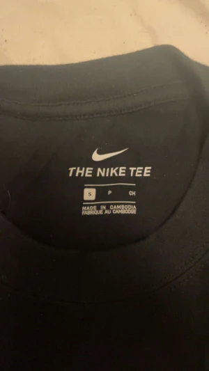 Svart Nike SB t-shirt med grafiskt tryck - Svart t-shirt från Nike SB i storlek S, med ett stilrent grafiskt tryck i vitt på ryggen och en sneaker-logga på bröstet. Klassisk rund hals och korta ärmar. Materialet är mjuk bomull som känns skönt mot huden. Perfekt för dig som gillar streetwear och snygga prints.