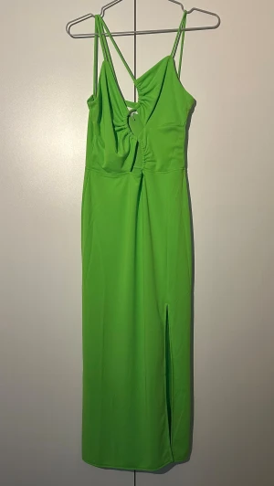 H&M grön klänning, storlek XS - Snygg grön långklänning från H&M med smala axelband och cool cut-out detalj framtill. Klänningen har en slits på ena sidan och är tillverkad i ett mjukt, stretchigt material som sitter skönt på kroppen. Perfekt för dig som vill sticka ut med en färgstark look.