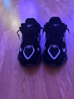 New Balance 9060 svarta sneakers - Säljer ett par New Balance 9060 sneakers i svart med vita detaljer. Skorna har chunky sula, mesh och mocka-paneler samt klassisk N-logga på sidan. Snygg och modern design med snörning och rund tå. Perfekta för dig som gillar streetwear och vill ha något bekvämt och stilrent.