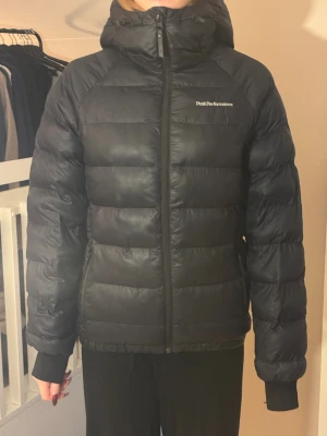 Svart Peak Performance dunjacka - Svart dunjacka från Peak Performance med huva och dragkedja framtill. Jackan har quiltad design, ribbade muddar. Perfekt för kalla dagar! finns kvitto! säljer pga jag växt ur den. Bara använt den 1 vinter så den är väldigt bra skick! skriv vid frågor💕nypris: 3250kr