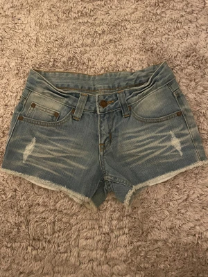 Ljusblå denimshorts - Säljer ett par snygga ljusblå denimshorts från Henry Como med slitna detaljer och fransig kant. Klassisk femficksmodell, broderi på bakfickorna och läderpatch med logga. Säljer pga att dem är för små för mig. Midjemått: 32cm. Skriv gärna vid frågor!!❤️❤️