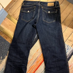 Mörkblå jeans från 157 - Mörkblå jeans med mid waist. Byxorna har raka ben och silverfärgade knappar på bakfickorna. Uppsydda lite på längden. Storlek M.