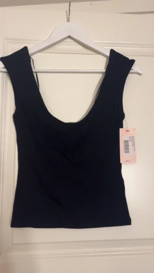 Svart ärmlös linnetopp från Nelly - Snygg svart linnetopp från Nelly med djup rundad urringning både fram och bak. Toppen är ärmlös och har en tight passform som framhäver siluetten. Perfekt att styla med jeans eller kjol för en clean look.