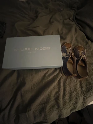 Philippe Models bytes mot andra skor el hoddies  - Säljer ett par snygga Philippe Model sneakers i blått och beige med coola detaljer. Skorna har snörning, rund tå och platt sula med PHILIPPE tryckt undertill. Materialet är mocka och skinn, vilket ger en lyxig känsla. Perfekt för dig som gillar stilrena och trendiga sneakers.