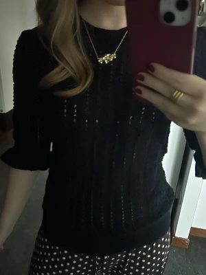 Svart stickad tröja Carin Wester XS - Svart stickad tröja från Carin Wester i storlek XS. Tröjan har ett snyggt hålmönster med vertikala ränder och trekvartsärmar med lätt volang vid ärmslutet. Rund halsringning och ribbad kant nedtill ger en cool och modern vibe.