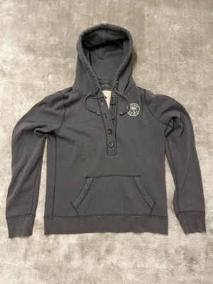 Mörkgrå hoodie Hollister med tryck - Grå hoodie från Hollister med tryck och vit markerad text på höger arm ”Hollister”                    | Size S/M | Längd 68 cm | Armlängd 70 cm Axelbredd 42 cm | Passar för 165-176 cm                     Hör gärna av dig vid frågor eller funderingar. Pris kan alltid diskuteras 😊.