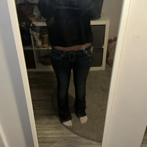 Mörkblå bootcut miss me jeans med detaljer - Säljer ett par mörkblå jeans från Miss Me med snygga kontrastsömmar och broderade bakfickor med nitar. Jeansen har låg midja och bootcut passform, vilket ger en schysst siluett. Materialet är klassisk denim med stretch för extra komfort.