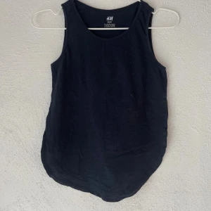 Svart linnetopp från H&M Basic - En enkel och stilren svart linnetopp från H&M Basic i mjuk bomull. Toppen är ärmlös med rundad hals och har en rak, något längre passform. Perfekt att matcha med jeans eller shorts för en clean look.